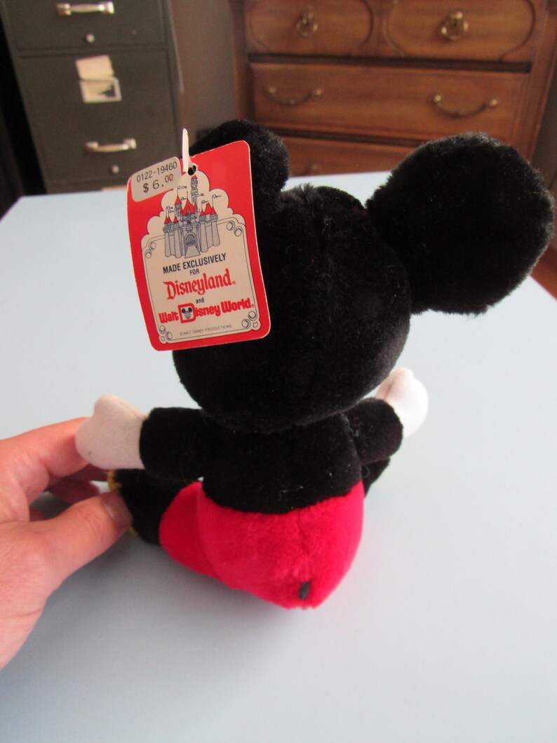 May include: A black plush Mickey Mouse toy with red shorts, white gloves, and large black ears. The toy has a red tag that reads "Made Exclusively For Disneyland and Walt Disney World."