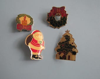 May include: Four Christmas-themed enamel pins. Designs include a wreath with a red bow, a candle with a red bow, a Santa Claus figure, and a Christmas tree with ornaments. All pins have gold-colored borders.