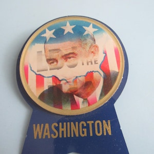 May include: Vintage political campaign button featuring a portrait of a man, possibly a politician, with the text "WASHINGTON" at the bottom. The button has a blue ribbon design with a gold border and stars.