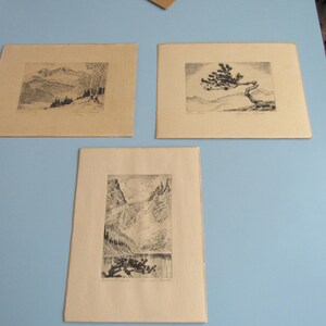 May include: Three black and white framed prints of nature scenes. The top left print shows a mountain range. The top right print shows a tree with branches reaching out. The bottom print shows a mountain range with a lake in the foreground.