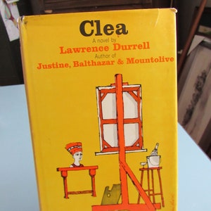 May include: A yellow book cover with the title "Clea" by Lawrence Durrell, author of Justine, Balthazar & Mountolive. The cover features an illustration of an easel with a painting on it, a small table with a woman's head on it, and a bottle of wine in a bucket.