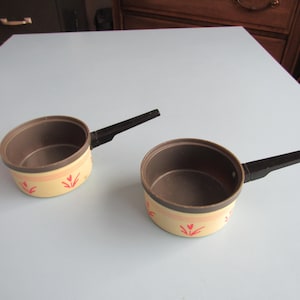 May include: Two small yellow and brown pots with black handles. The pots have a red floral design.