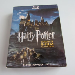 May include: A Blu-ray set of the complete Harry Potter 8-film collection. The box features a dark, dramatic image of Hogwarts Castle on a rocky cliffside, with the title in a stylized font. The set includes 8 discs.
