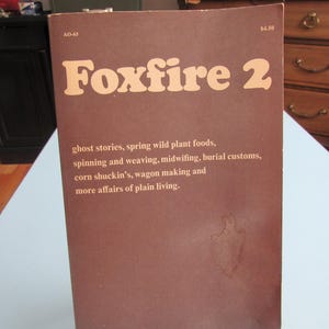 May include: A brown paperback book titled Foxfire 2 with the subtitle ghost stories, spring wild plant foods, spinning and weaving, midwifing, burial customs, corn shuckin's, wagon making and more affairs of plain living. The cover has a stain.