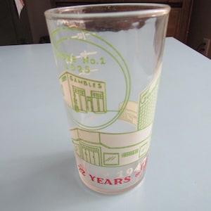 May include: A clear glass with a green and white design. The glass features the text "Store No. 1 1925" and "Gambles" in green, with the words "22 Years of 1947" in red. The glass is cylindrical and appears to be vintage.