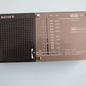 May include: A vintage black and gray Sony Tick-Talk voice synthesizer clock radio. The radio features an FM/AM tuner, a digital display, and a speaker grill. The text "SONY" is visible on the top left. The radio has a snooze function.