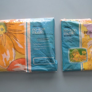 May include: Two packages of no-iron muslin bedding featuring a large orange and yellow floral pattern. The packaging includes the text Fashion Manor, no-iron muslin, 50% Fortrel polyester, 50% cotton, and a finished size of 81 inches by 96 inches.