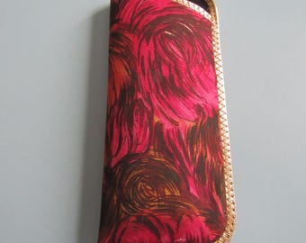 May include: A rectangular eyeglass case with a vibrant, abstract pattern in shades of pink, red, and brown. The case is trimmed with a gold-colored decorative border. The case is closed.