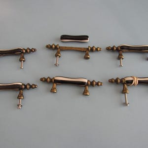 May include: A set of five drawer pulls and one loose handle insert. Each pull features a dark brown and cream-colored center bar with antique brass-toned metal ends and mounting posts. One handle has a small rubber band wrapped around it.