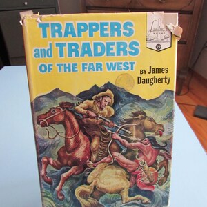 May include: A vintage hardcover book titled "Trappers and Traders of the Far West" by James Daugherty. The cover features a colorful illustration of cowboys on horseback, with a yellow background and blue text.
