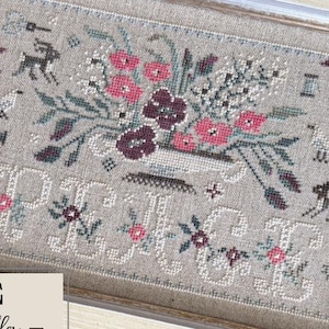 May include: Framed cross-stitch sampler with a floral design in pink, burgundy, and green. The word "PEACE" is stitched below the flowers. The sampler is in a light-colored wooden frame.