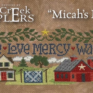 May include: Cross-stitch sampler with the text "Seek Justice, Love Mercy, Walk Humbly." The design features a rural landscape with houses, trees, a church, and a person with a dog. The words "Micah's Mission" are also displayed.