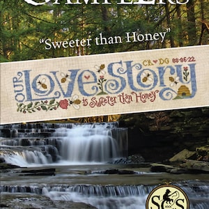 May include: A cross-stitch pattern featuring the words "Our Love Story is Sweeter Than Honey" with a beehive, bees, and flowers. The pattern is displayed on a beige fabric with a waterfall in the background.