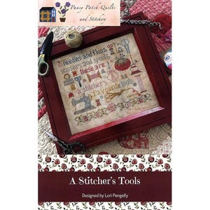 May include: A framed cross-stitch sampler with the text "A Stitcher's Tools." The sampler features images of sewing tools, including scissors, needles, and a sewing machine. The frame is a dark red color, and the background is a floral pattern.
