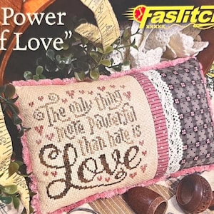 May include: A decorative pillow with the text "The only thing more powerful than hate is Love" in brown stitching. The pillow has a pink border and a patterned section with white lace. The words "Power of Love" are above the pillow.