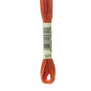 May include: A single skein of orange embroidery floss, color 921, against a white background. The floss is wrapped with a white and green label that includes a barcode. The color is a warm, earthy tone.