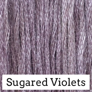 May include: Close-up of Sugared Violets yarn. The yarn is a blend of lavender and white, creating a textured, heathered appearance. The text "Sugared Violets" is displayed in a white rectangle at the bottom of the image. This yarn is suitable for various crafting projects.