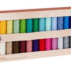 May include: A box set of colorful sewing thread spools. The spools are arranged in two rows, showcasing a spectrum of colors from yellow to black. The box has the brand name "Metter" and text that reads "HETROSENE".