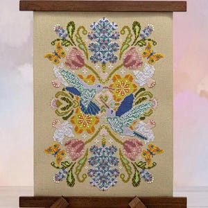 May include: A framed cross-stitch featuring two hummingbirds facing each other, surrounded by flowers and butterflies. The design includes pink tulips, blue and white flowers, and orange butterflies on a beige background. The frame is made of dark wood.