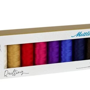 May include: A box set of Mettler quilting thread in various colors. The box is white with gold trim and features the word "Quilting" and the Mettler logo. The thread spools are in shades of gold, red, pink, purple, blue, navy, and brown.