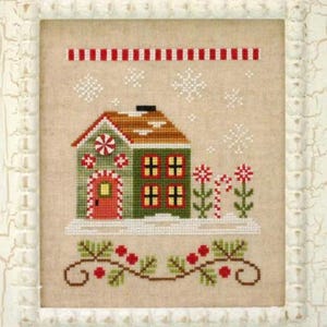 May include: Cross-stitch design of a festive house with a red door and green walls, adorned with candy cane accents and snowflakes. The design is framed in a white, distressed-look frame, with a red and white striped border at the top and a garland at the bottom.