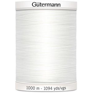 May include: A spool of white Gütermann thread. The spool is cylindrical with a white label at the top and bottom. The text "Gütermann" is printed on the top label. The bottom label reads "1000 m - 1094 yds/vgs".