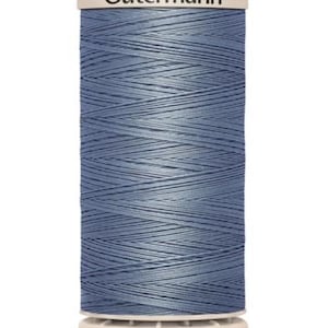 May include: A spool of Gutermann thread in a muted blue color. The thread is tightly wound, creating a textured surface. The top of the spool features the Gutermann brand name in a clean, sans-serif font. Ideal for sewing and crafting projects.