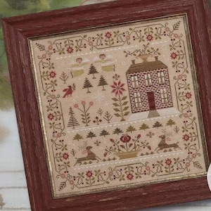 May include: A framed cross-stitch sampler titled The Light of Winter by Brenda Gervais, featuring a brick house, deer, angels, and pine trees in red, green, and tan thread on a beige fabric background, enclosed in a rustic dark red wooden frame.