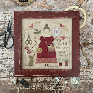 May include: A cross-stitch pattern booklet featuring a woman with a needle and thread, a cat, and the text "My heart is fed with needle & thread". The pattern is titled "Fed" and is available for wholesale for $7.00. The booklet is 8.5 inches by 11 inches.