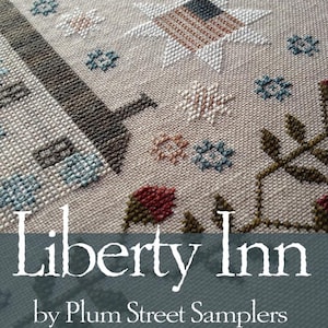 May include: Close-up of a cross-stitch sampler with a beige background. The design includes a star with an American flag pattern, floral motifs, and the text "Liberty Inn" by Plum Street Samplers.