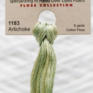 May include: A skein of green and yellow cotton floss labeled "1183 Artichoke" with a tag that reads "5 yards". The floss is part of a "Floss Collection" specializing in hand-over-dyed fibers.