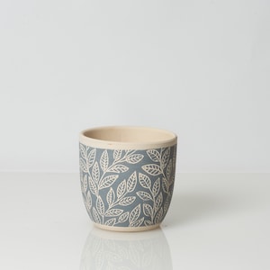 May include: A gray ceramic planter with a white leaf pattern. The planter is round and has a smooth finish.
