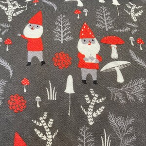 May include: A gray fabric with a repeating pattern of red and white gnomes, red and white mushrooms, and gray trees. The gnomes are wearing red hats and have white beards. The mushrooms have red tops and white stems. The trees are stylized and have a gray color.