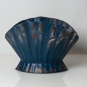 May include: A blue metal planter shaped like a seashell with a distressed finish. The planter has a wide, open top and a rounded base.