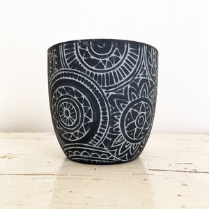 Op de afbeelding: Een zwarte keramische pot met een wit geometrisch patroon. De pot heeft een ronde vorm en een gladde afwerking.