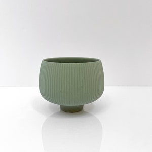 May include: A small, green ceramic planter with a ribbed design and a rounded base.