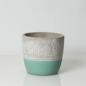 Może przedstawiać: Szara betonowa doniczka z białym wzorem drzewa i turkusowym dnem.