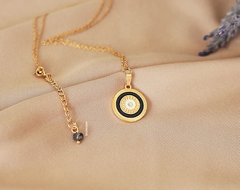 Puede incluir: Collar de oro con un colgante de ojo turco negro y blanco. El colgante tiene un borde dorado y un centro blanco con un ojo azul.