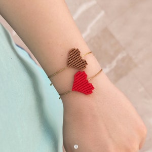 May include: A gold bracelet with two heart-shaped charms. One charm is red and the other is brown.