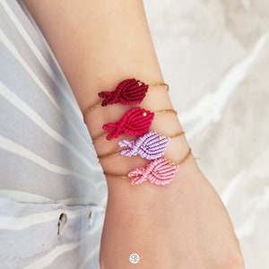 Peut inclure: Quatre bracelets d'amitié colorés avec des breloques en forme de poisson. Les bracelets sont faits d'un cordon doré et présentent des breloques en forme de poisson rouge, rose et violet.