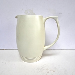以下が含まれることがあります： クリーム色のセラミックピッチャー。曲線的なハンドルと注ぎ口が付いています。ピッチャーは滑らかで丸みを帯びたボディで、底の近くには一連の水平線があります。ハンドルはシンプルで曲線的なデザインです。白い背景に配置されています。