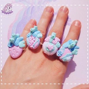 May include: Four pastel pink and blue anatomical heart rings with intricate details. The rings are worn on a hand, showcasing the unique design of each piece.