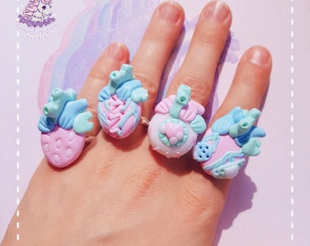 May include: Four pastel pink and blue anatomical heart rings with intricate details. The rings are worn on a hand, showcasing the unique design of each piece.