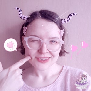 May include: A person wearing pink glasses and a pink sweater with a black and white octopus hair clip. The person is winking and has a pink heart with the word "love" written in Japanese on the side of their face.