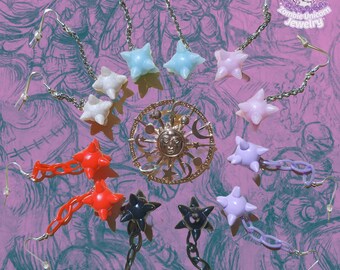 May include: A collection of star-shaped earrings in various colors, including white, light blue, pink, red, black, and purple. The earrings are connected to silver chains and hooks. A gold-colored sun and moon pendant is in the center. The background is a patterned purple.