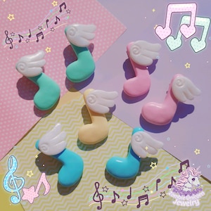 May include: A collection of colorful, musical note charms with white angel wings. The charms are in various pastel colors, including teal, pink, yellow, and blue. The background is a mix of pink and purple with musical notes and star decorations.