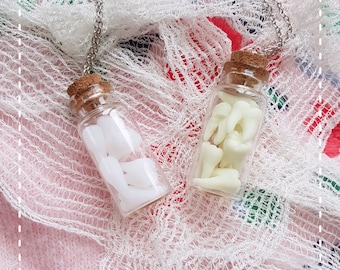 May include: Two silver chains with glass vials filled with white teeth charms. The vials have cork stoppers and are hanging from the chains.