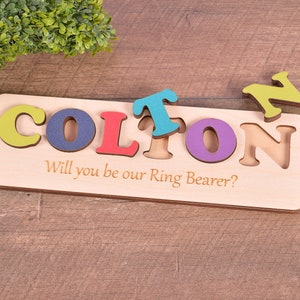 May include: Wooden puzzle with the name COLTON cut out and colorful letters to fit in the spaces. The puzzle also says "Will you be our Ring Bearer?"