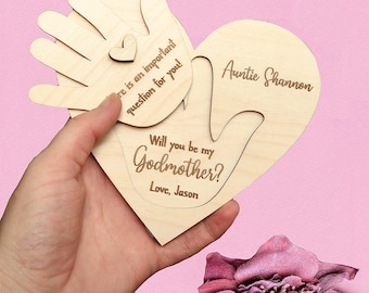 Può includere: Carta di legno a forma di cuore con un ritaglio a forma di mano, che chiede "Vuoi essere la mia madrina?" con il testo "Con affetto, Jason" e "Zia Shannon" sulla carta.