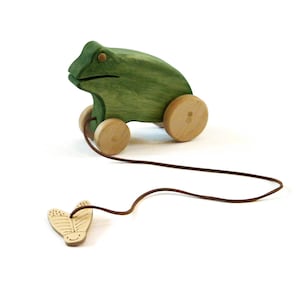 May include: A green wooden frog pull toy with brown wheels and a brown string attached to a wooden butterfly.